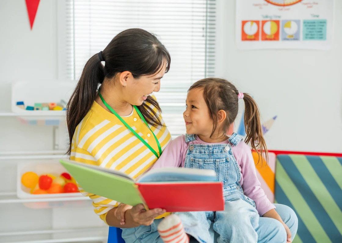 Teacher reading with young child in classroom.